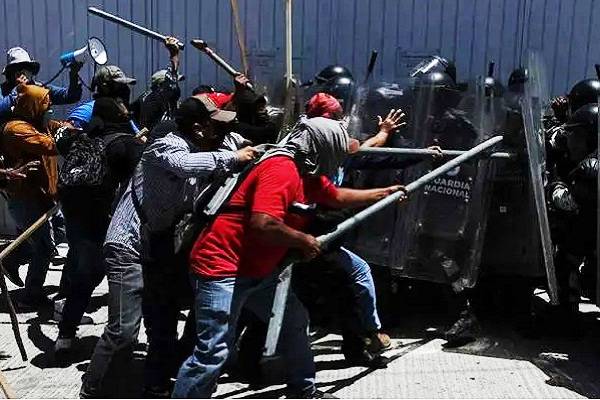 Armados con palos de kendo, miembros de la CNTE se lanzan violentamente contra instalaciones que resguardan boletas electorales. Guardia Nacional lo impide